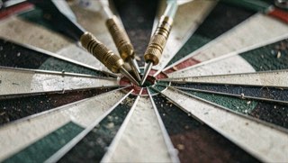 Drie dartpijlen dicht bij elkaar in het bord, de metalen scheiding tussen de vakken scherp in beeld.