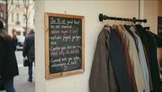 Klein bord met handgeschreven tekst aan een cafémuur naast een kapstok met jassen eronder.