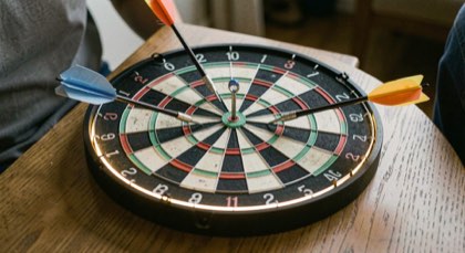 Dartbord met zwarte omranding onder een ring van licht, drie pijlen in de twintig.